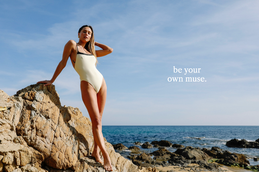mannequin maillot de bain blanc et noir debout sur un massif rocheux devant la mer avec un text be your own muse